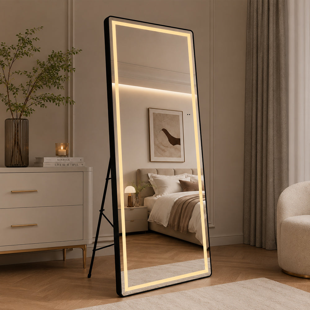 Helfigur spejl med LED-lys og sort ramme 65x165 cm står tændt på gulvstativ i soveværelse